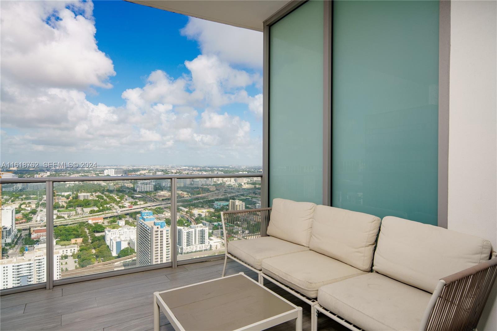 A high-rise balcony features a white sofa, a small table, and panoramic city views — 851 NE 1st Ave # 4406, Miami FL 33132, MIAMI, FL