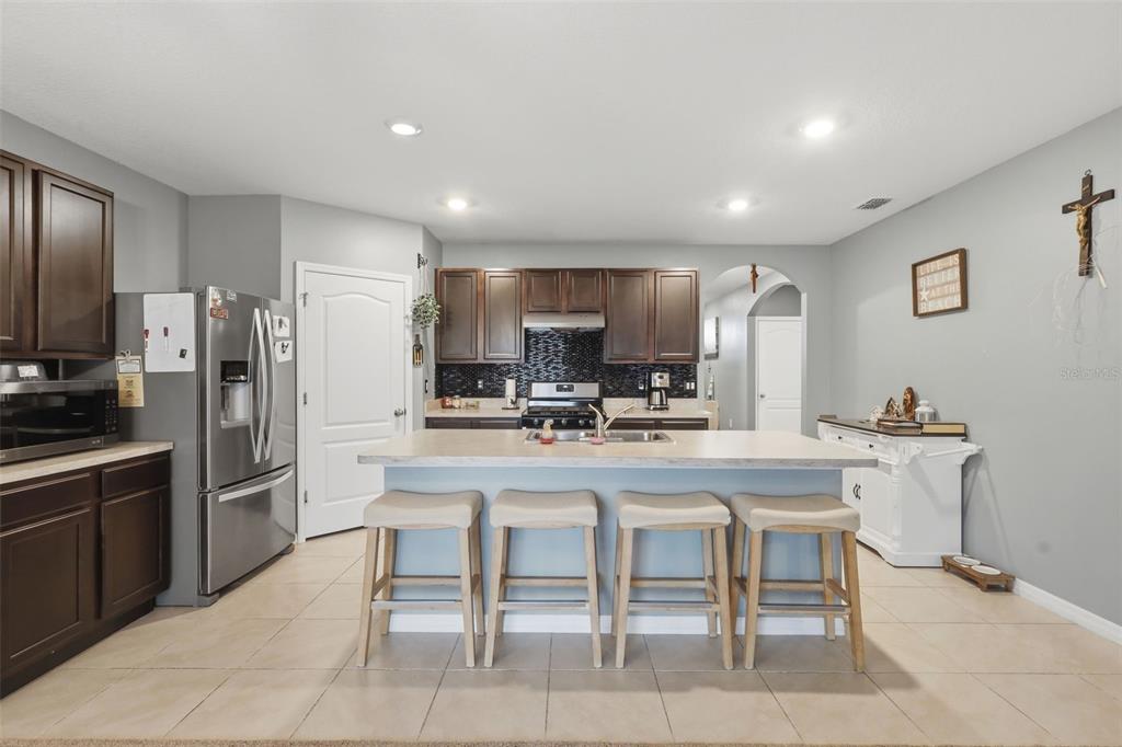 A kitchen features dark wood cabinets, stainless steel appliances, a central island, and tiled floors — 3871 BRANT PLACE, LEESBURG, FL