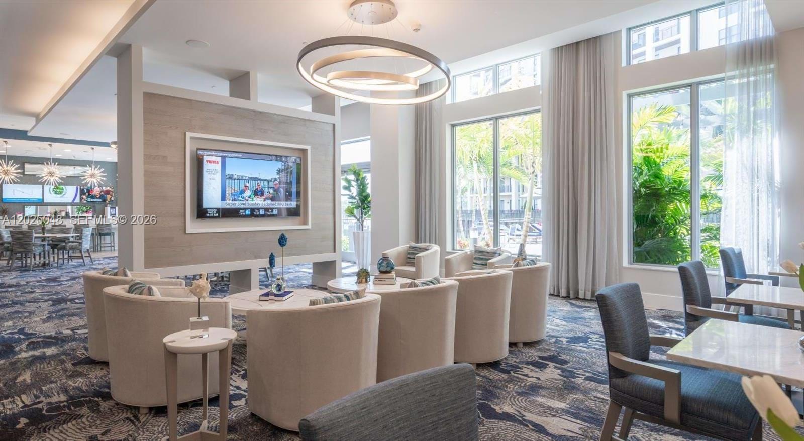 A modern lounge area features a central television, circular light fixture, and floor-to-ceiling windows — 4720 NW 85th Ave, Doral FL 33166, DORAL, FL
