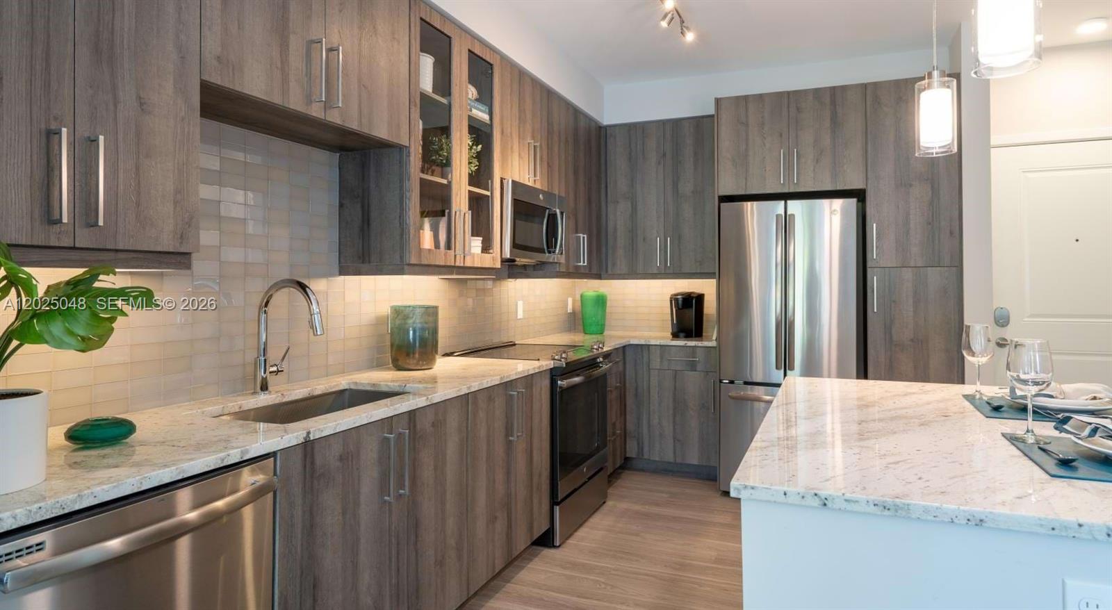 A modern kitchen features wood-grain cabinets, stainless steel appliances, and light-colored granite countertops — 4720 NW 85th Ave, Doral FL 33166, DORAL, FL