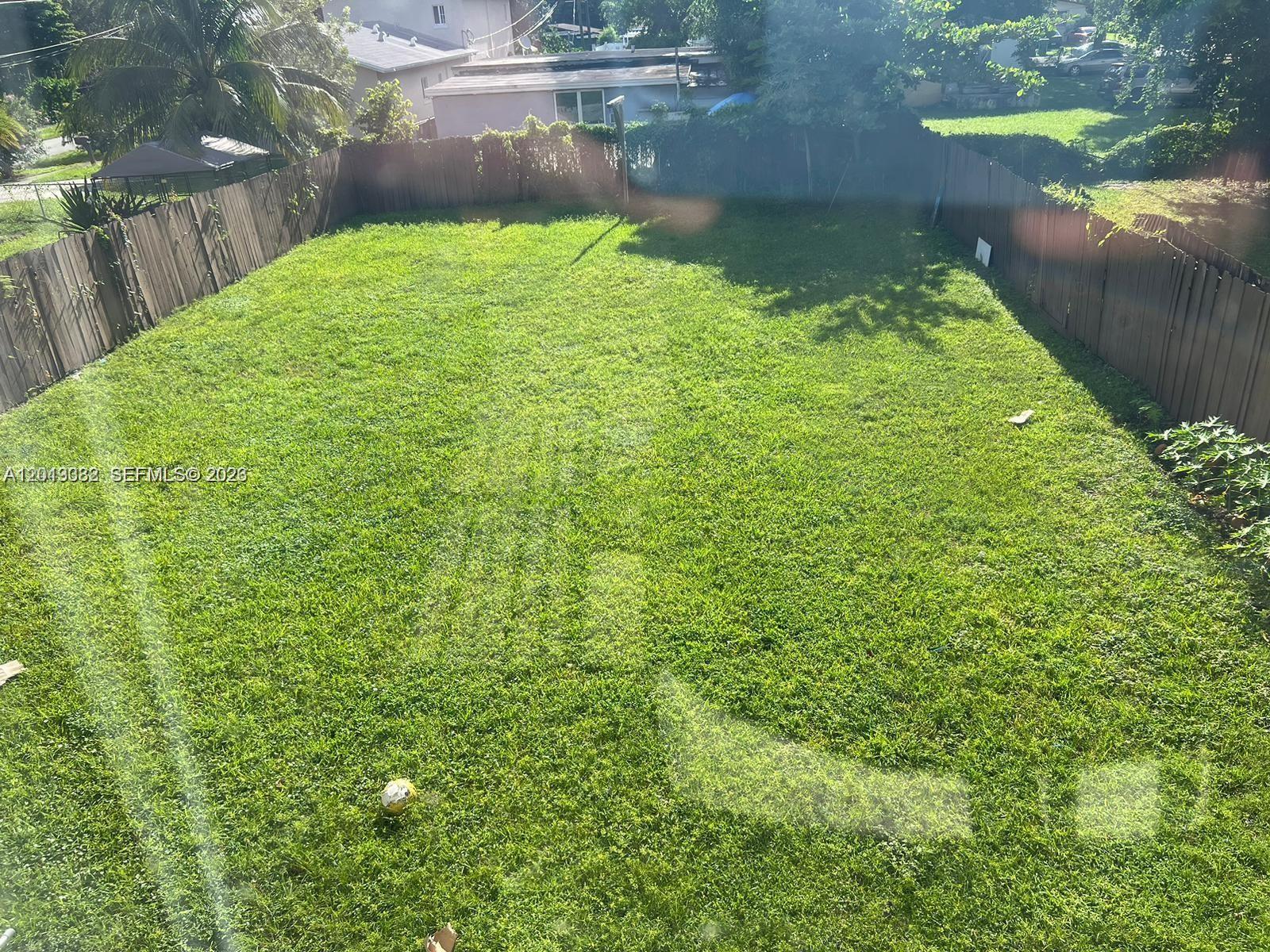 A large, rectangular backyard features a green lawn enclosed by a wooden fence — 4245 NW 24th Ave, Miami FL 33142, MIAMI, FL
