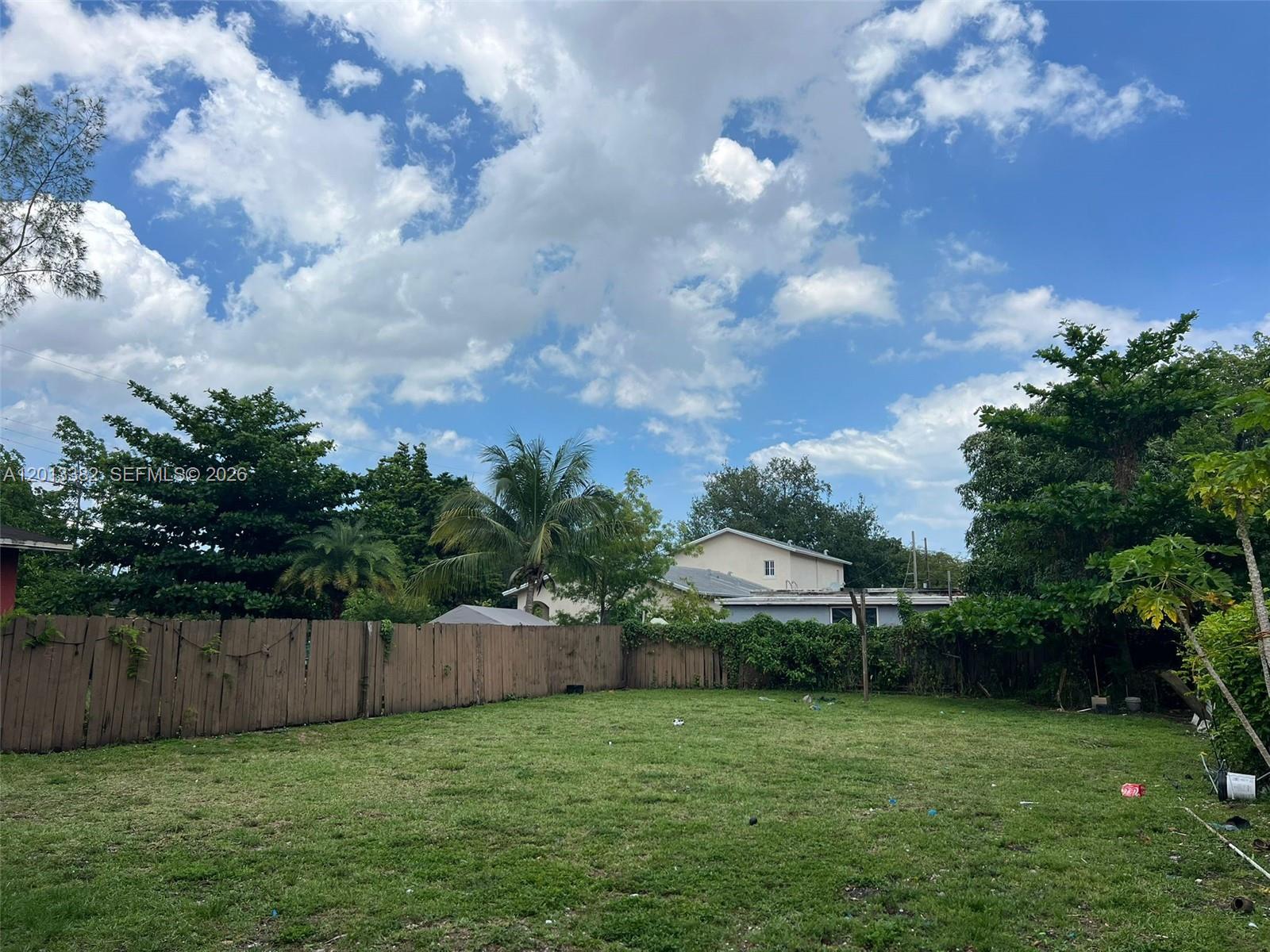 A grassy backyard features a wooden fence, surrounding trees, and a house in the background — 4245 NW 24th Ave, Miami FL 33142, MIAMI, FL