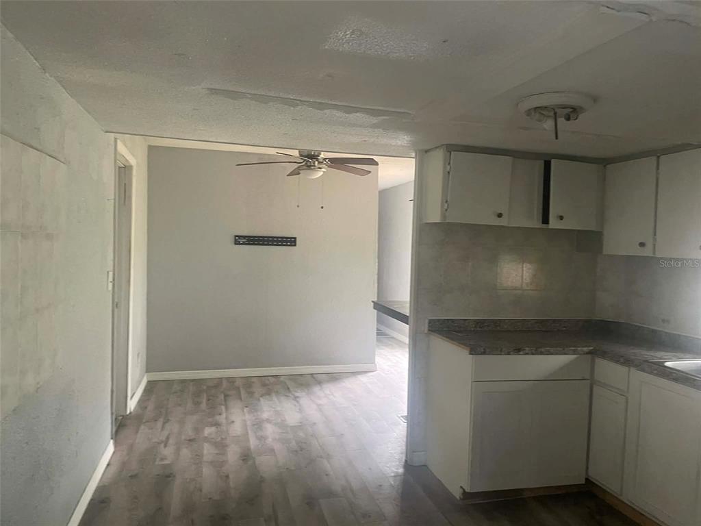 A kitchen with white cabinets and gray flooring opens into a dining area with a fan — 8716 N TANGERINE PLACE, TAMPA, FL