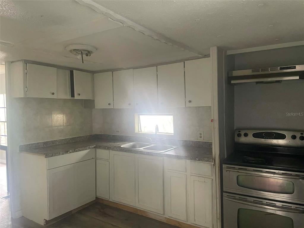 A kitchen features white cabinets, a double-basin sink, laminate countertops, and a stainless steel stove — 8716 N TANGERINE PLACE, TAMPA, FL