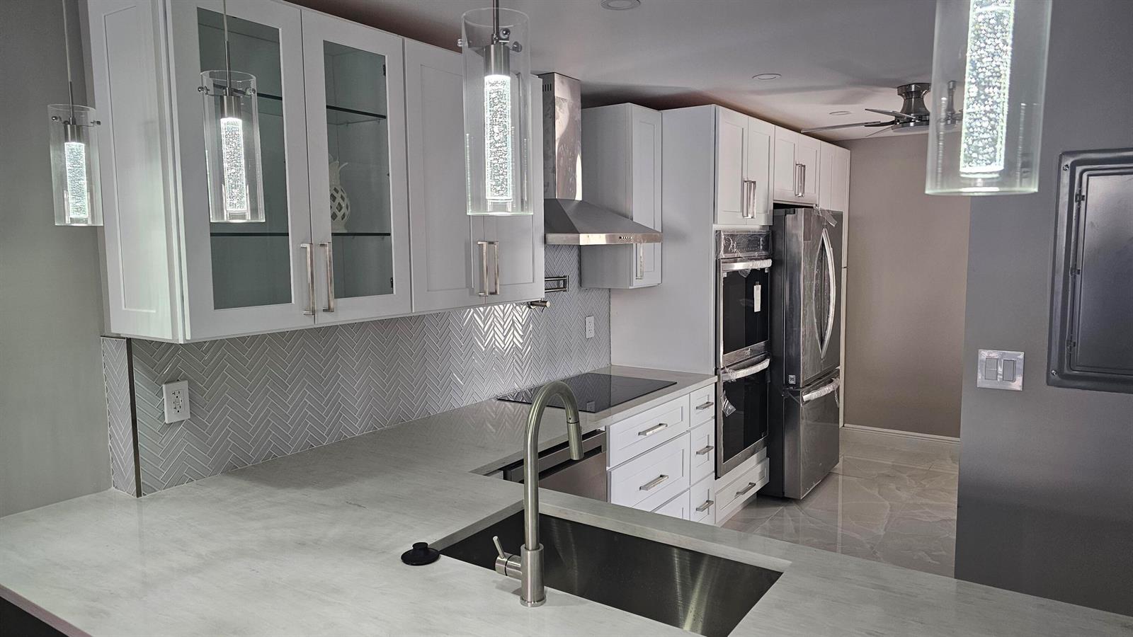 A modern kitchen features white cabinets, stainless steel appliances, a herringbone backsplash, and pendant lighting — 1 Royal Palm Way # 101, Boca Raton FL 33432, BOCA RATON, FL