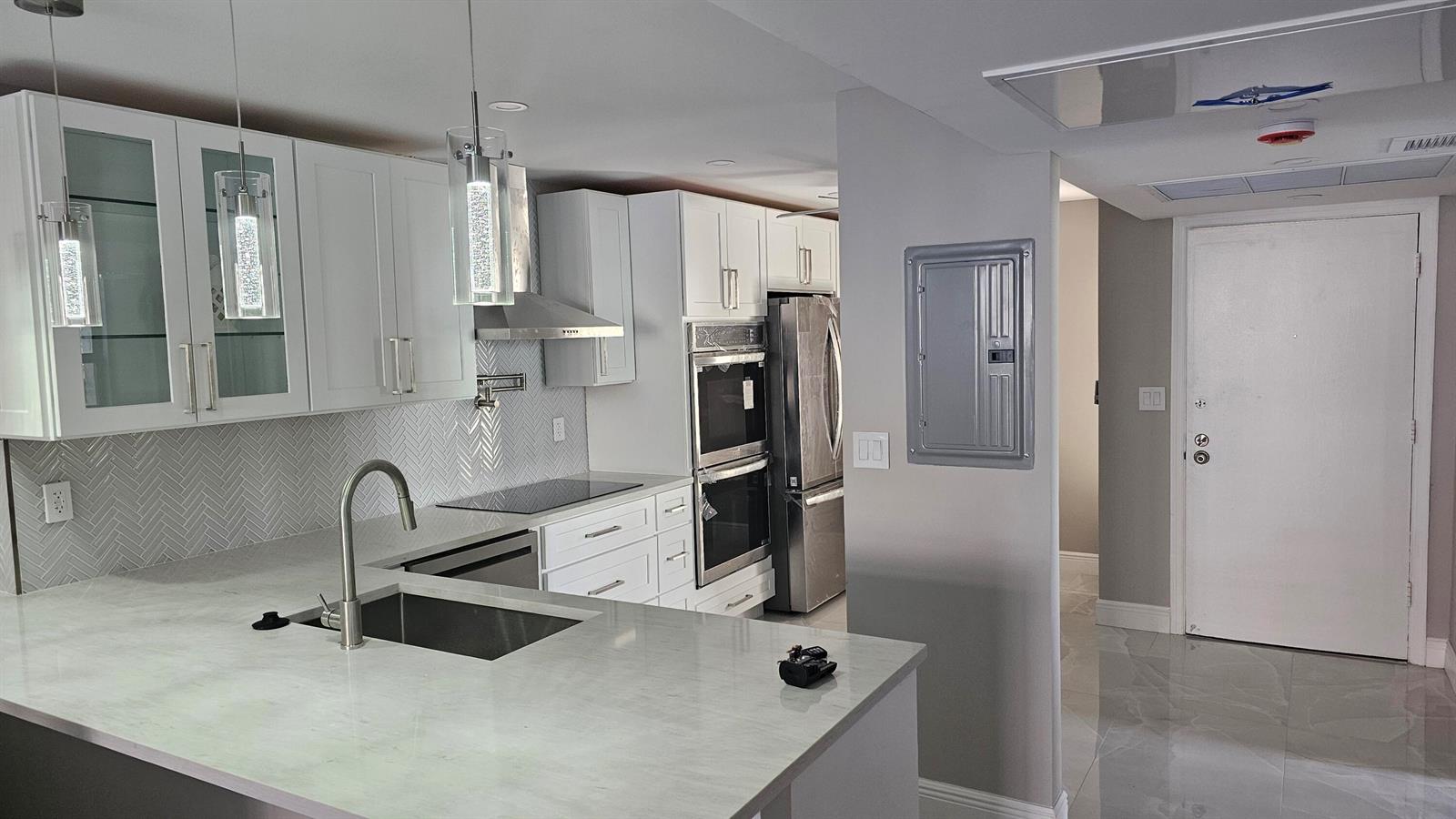 A modern kitchen features white cabinetry, stainless steel appliances, a herringbone backsplash, and quartz countertops — 1 Royal Palm Way # 101, Boca Raton FL 33432, BOCA RATON, FL