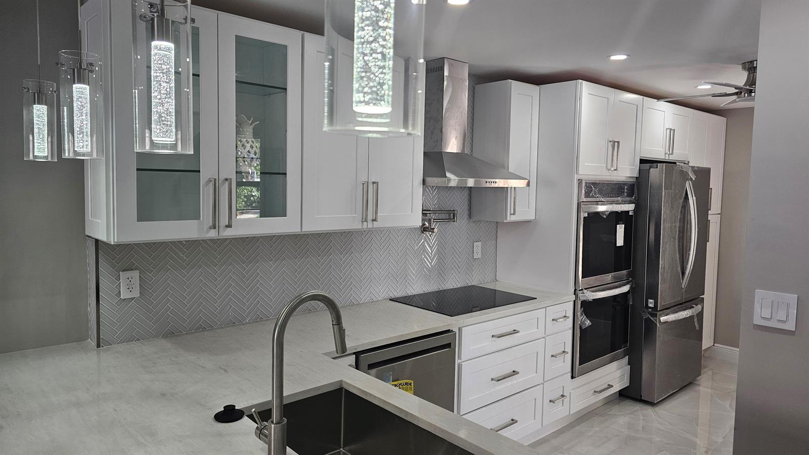 A modern kitchen features white cabinets, stainless steel appliances, and a gray herringbone tile backsplash — 1 Royal Palm Way # 101, Boca Raton FL 33432, BOCA RATON, FL