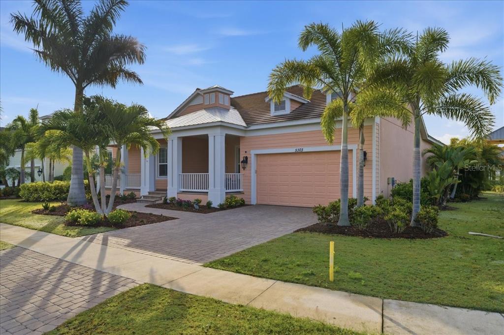 A peach-colored house with a front porch, a two-car garage, and several palm trees — 5303 FISHERSOUND LANE, APOLLO BEACH, FL