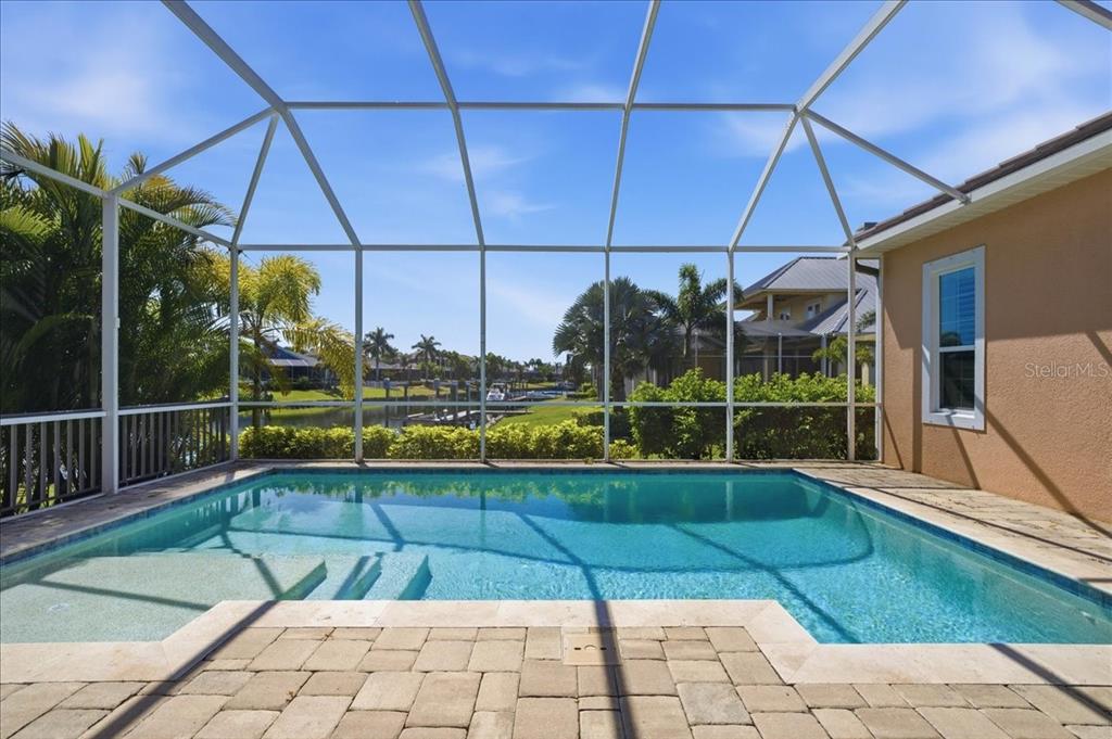 A screened-in swimming pool with a stone patio overlooks a canal and neighboring houses — 5303 FISHERSOUND LANE, APOLLO BEACH, FL