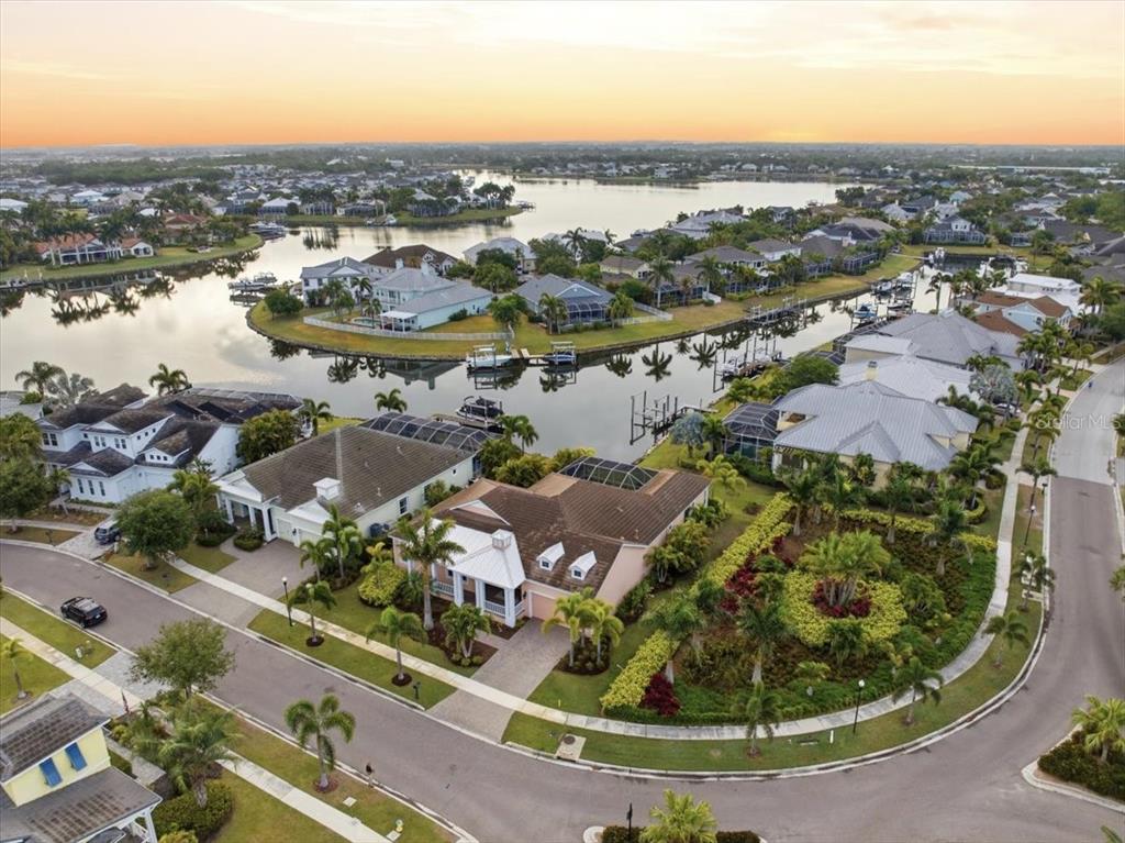 An aerial view shows waterfront houses with swimming pools and boat docks at sunset — 5303 FISHERSOUND LANE, APOLLO BEACH, FL