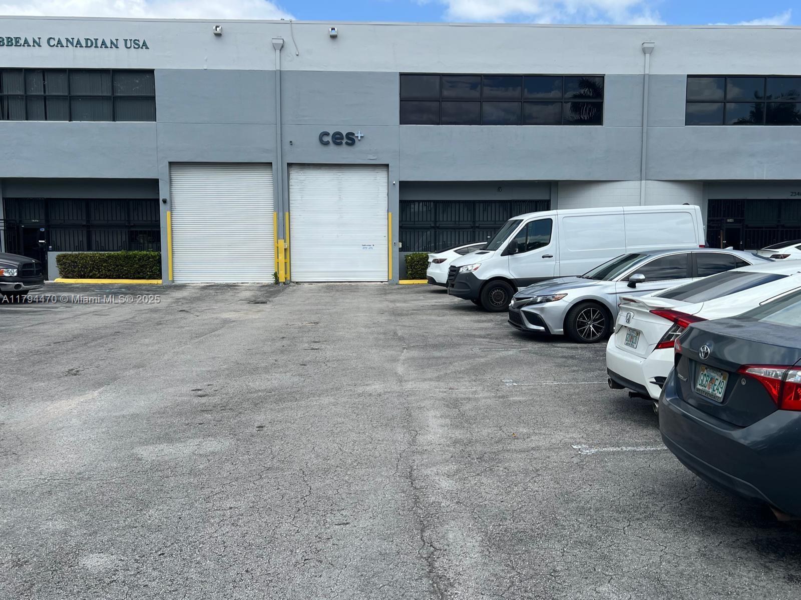 The exterior of a commercial warehouse building features two roll-up doors and a parking lot — 2330 NW 102nd Pl, Doral FL 33172, DORAL, FL