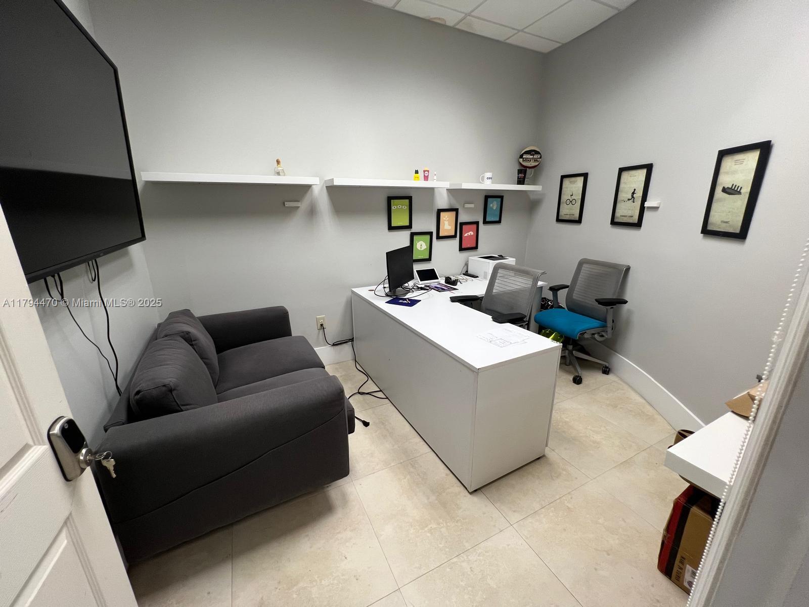 A small office features a grey sofa, a white desk, two chairs, and wall-mounted shelves — 2330 NW 102nd Pl, Doral FL 33172, DORAL, FL
