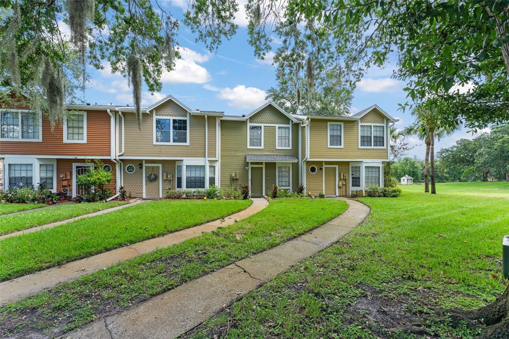 A row of multi-story townhomes with tan and brown siding and curved concrete walkways — 11715 WINDBOURNE COURT, ORLANDO, FL