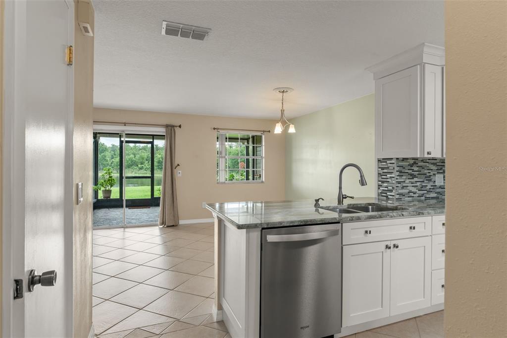 A kitchen with white cabinets and granite countertops opens into a living area with tile — 11715 WINDBOURNE COURT, ORLANDO, FL