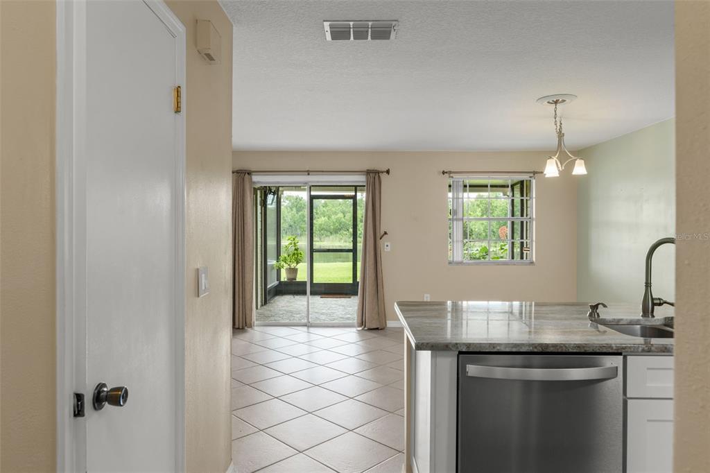 A kitchen island with a sink overlooks a tiled living area with a screened patio — 11715 WINDBOURNE COURT, ORLANDO, FL