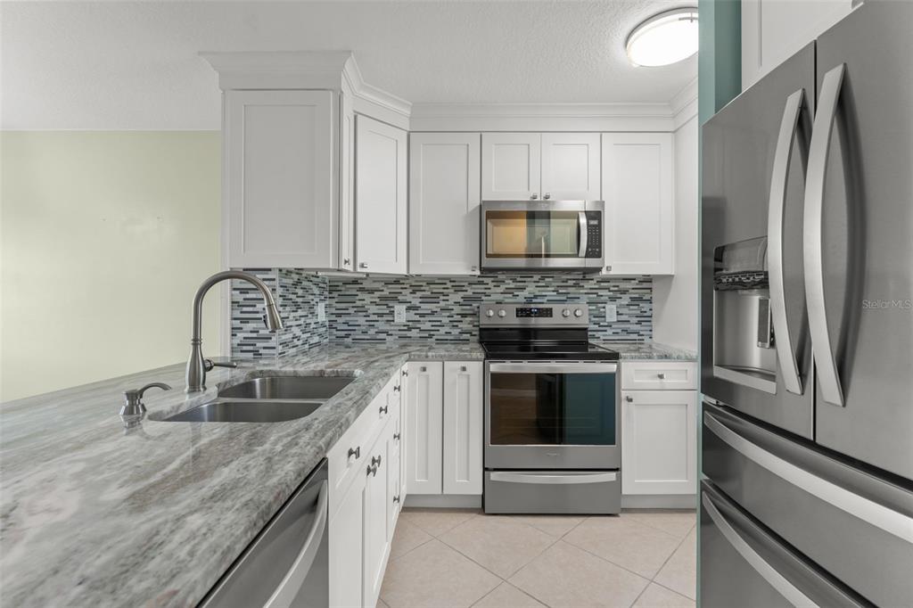A kitchen features white cabinets, stainless steel appliances, and a gray granite countertop — 11715 WINDBOURNE COURT, ORLANDO, FL