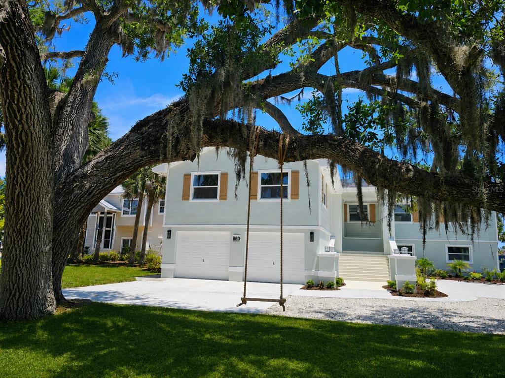 A two-story light green house with a two-car garage sits behind a large oak tree — 860 LAMBERT AVENUE, FLAGLER BEACH, FL