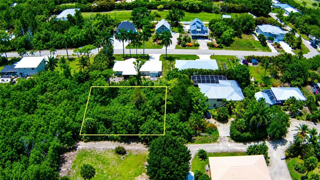 An aerial view shows a rectangular vacant lot outlined in yellow amidst a residential neighborhood — 7455 GEORGIANA DRIVE, BOKEELIA, FL