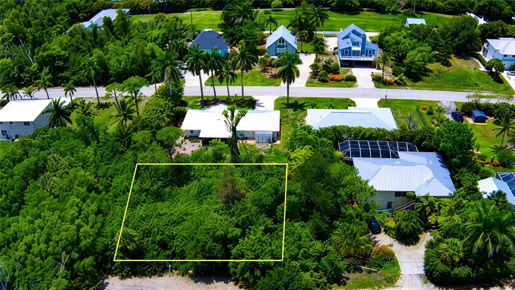 An aerial view shows a rectangular, tree-covered vacant lot outlined in yellow near residential houses — 7455 GEORGIANA DRIVE, BOKEELIA, FL