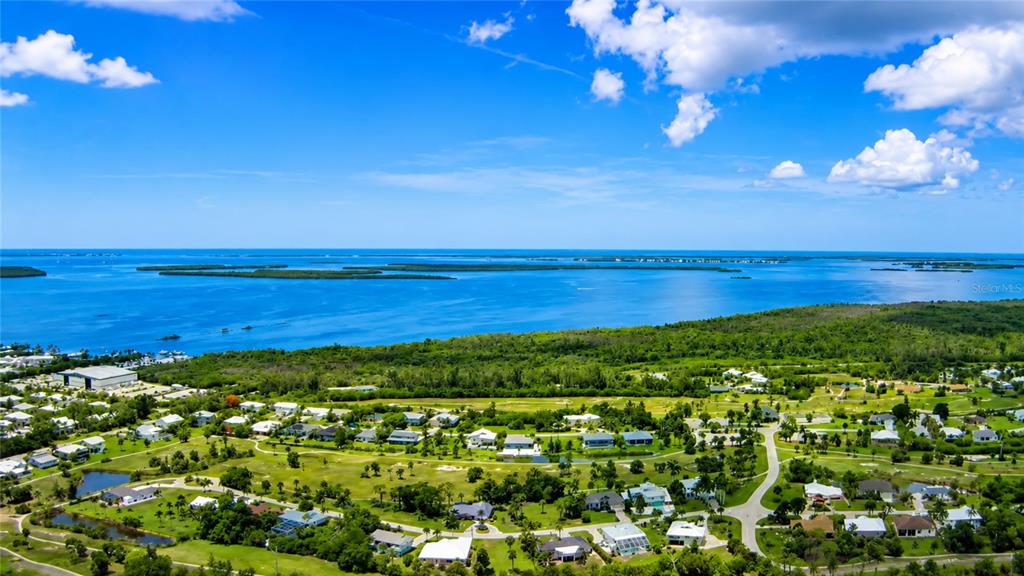 An aerial view shows a coastal residential community with houses, green spaces, and a large bay — 7455 GEORGIANA DRIVE, BOKEELIA, FL