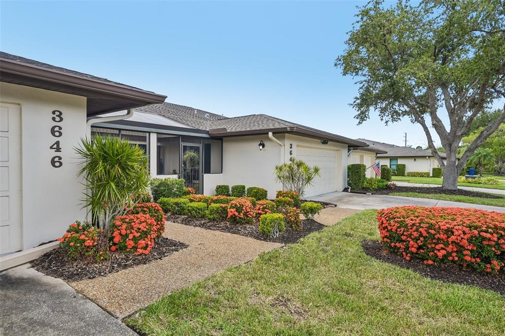 A single-story house exterior features a beige facade, a concrete walkway, and vibrant orange landscaping — 3646 GLENEAGLE DRIVE UNIT 10B, SARASOTA, FL