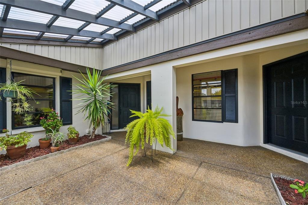 A covered outdoor courtyard features a concrete patio, potted plants, and dark-framed doors and windows — 3646 GLENEAGLE DRIVE UNIT 10B, SARASOTA, FL