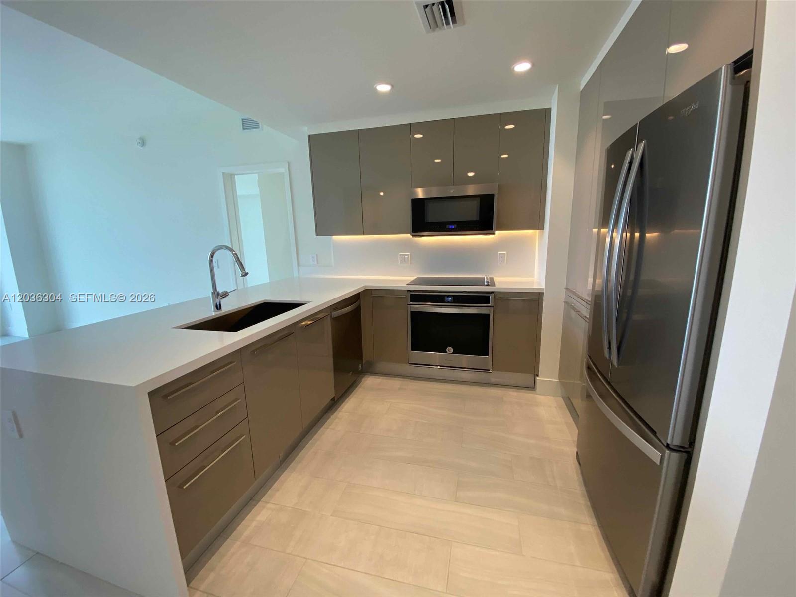 A modern kitchen features glossy taupe cabinets, stainless steel appliances, and white quartz countertops — 2000 Metropica Way # 307, Sunrise FL 33323, SUNRISE, FL