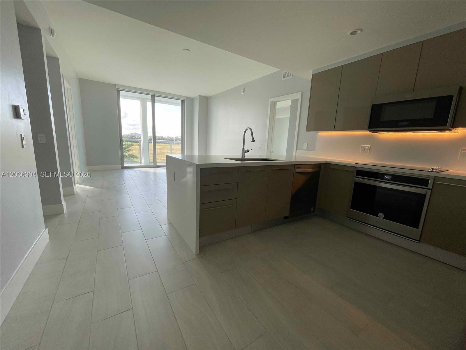 A modern kitchen features light-colored tile floors, a white island, and stainless steel appliances — 2000 Metropica Way # 307, Sunrise FL 33323, SUNRISE, FL