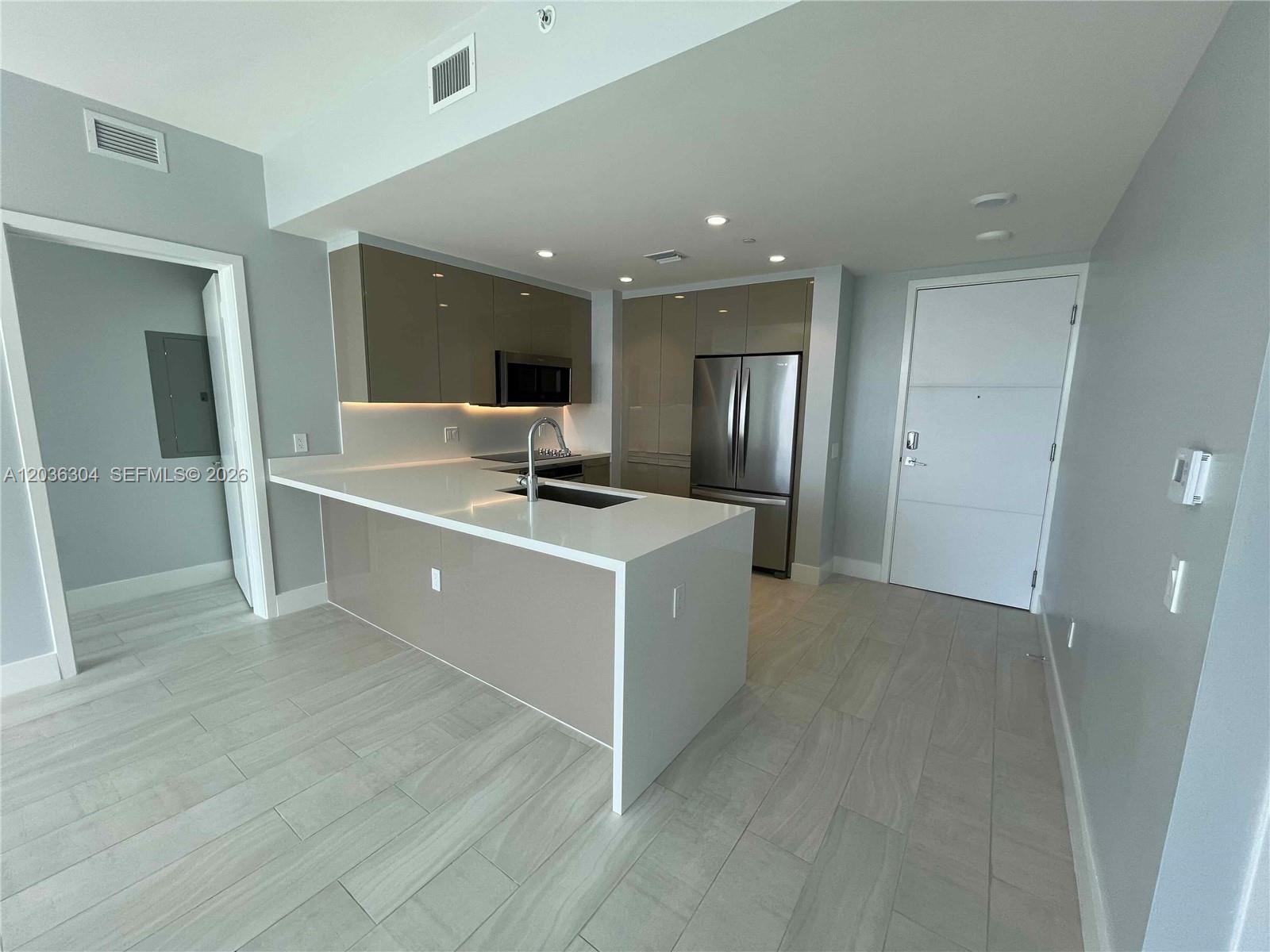 A modern kitchen features glossy taupe cabinets, white countertops, and light-colored tile flooring — 2000 Metropica Way # 307, Sunrise FL 33323, SUNRISE, FL