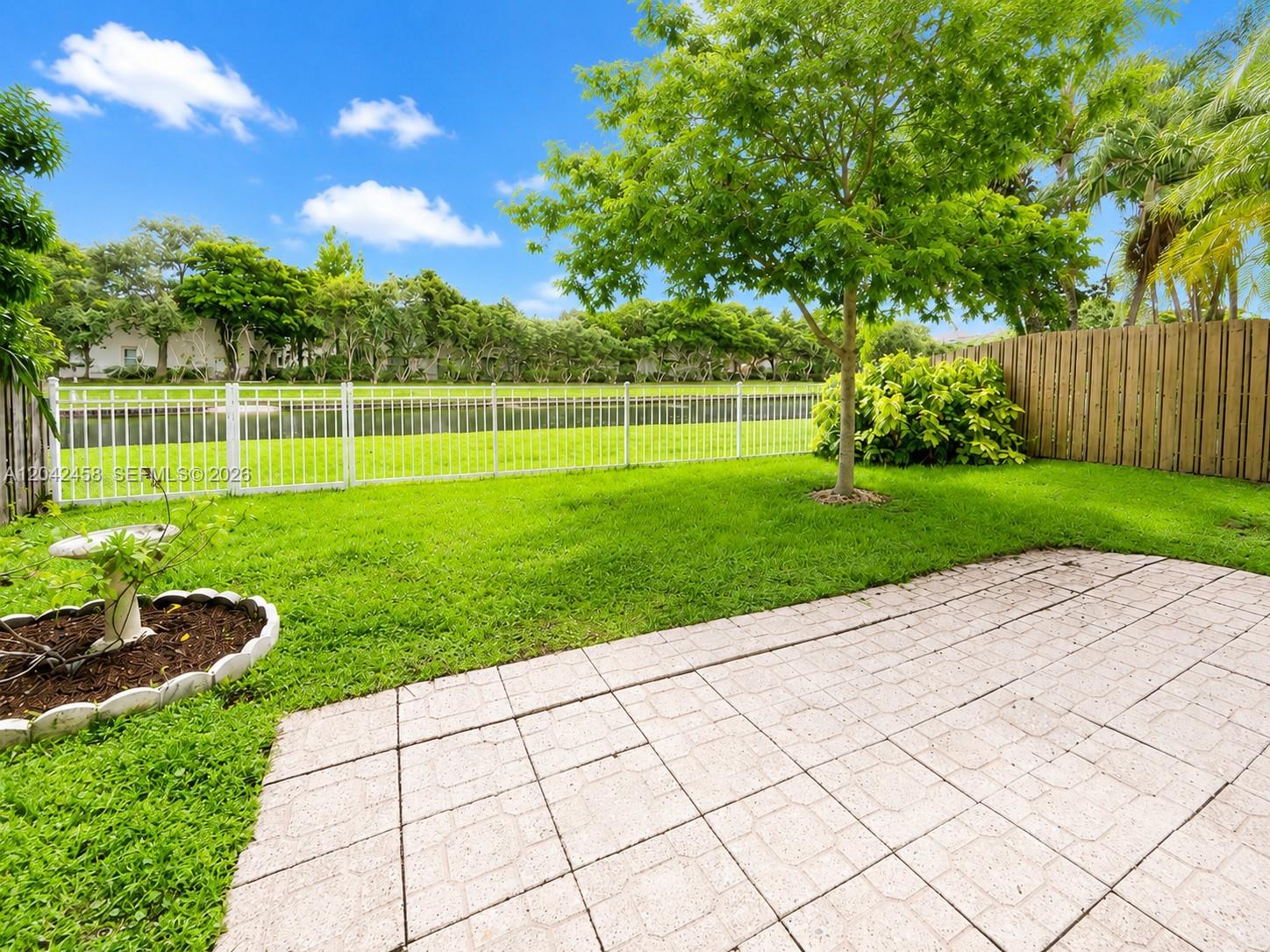 A backyard features a paved patio, a grassy lawn, a tree, and a white fence — 10750 NW 10th St, Plantation FL 33322, PLANTATION, FL