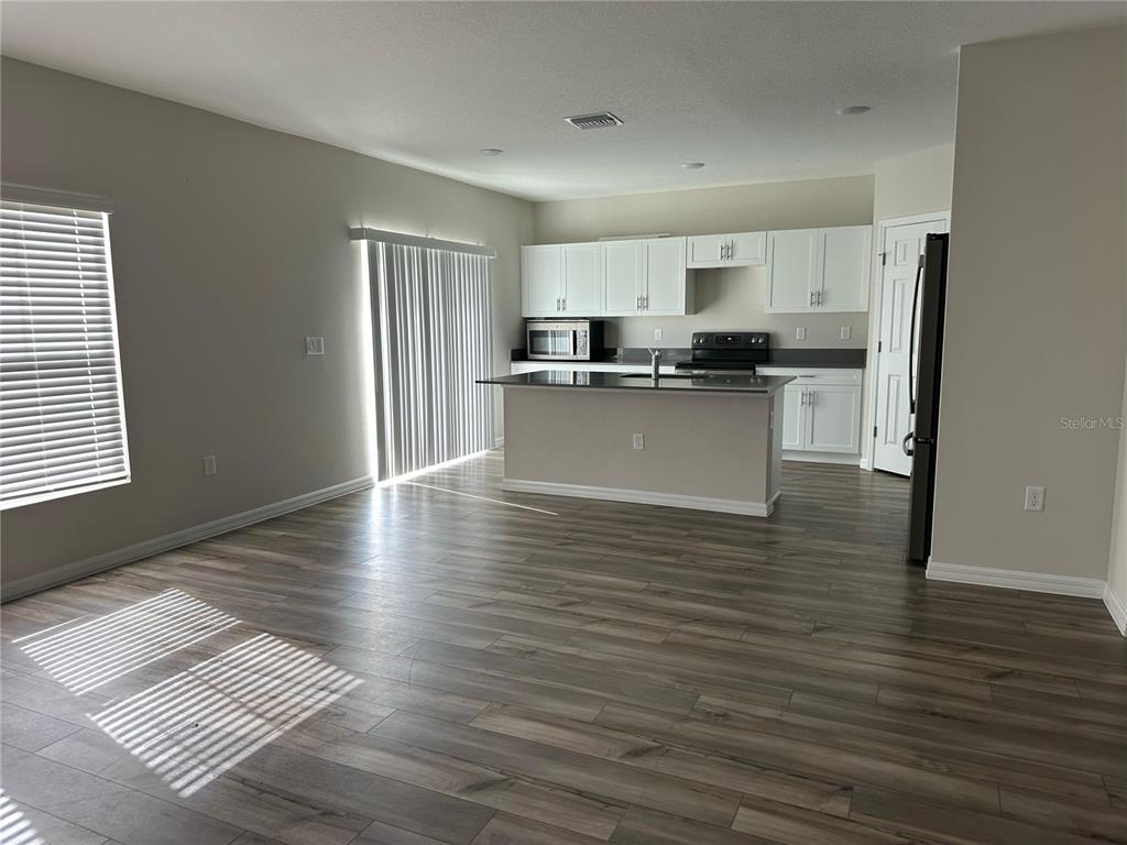 An open-concept kitchen features white cabinetry, a central island, and wood-look flooring — 1572 ELLESMERE AVENUE, HAINES CITY, FL