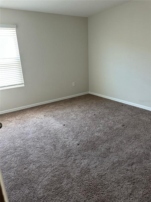 An empty bedroom features beige walls, white trim, a window with blinds, and brown carpeting — 1572 ELLESMERE AVENUE, HAINES CITY, FL