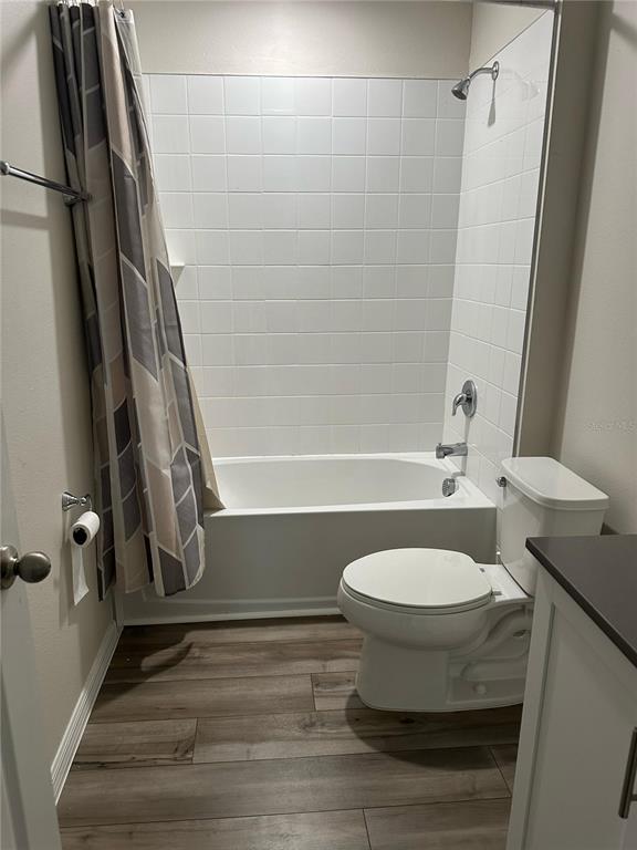 A bathroom features a white tiled shower-tub combination, a toilet, and wood-look flooring — 1572 ELLESMERE AVENUE, HAINES CITY, FL