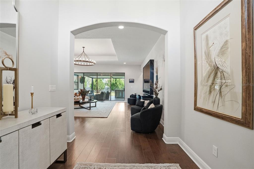 A view through an arched entryway into a living room with hardwood floors and patio doors — 1916 JULLEE LANE, PALM HARBOR, FL