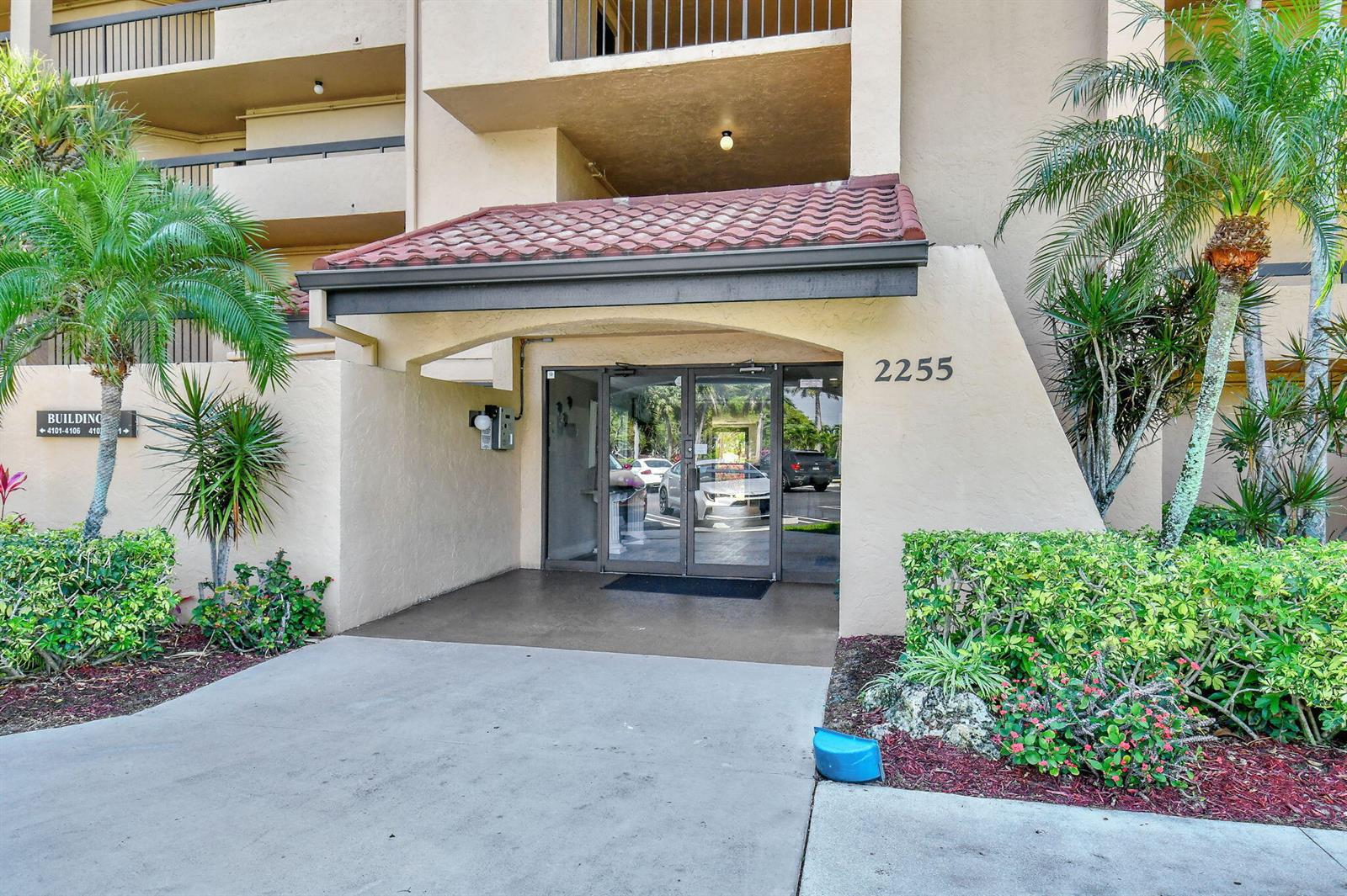 The exterior entrance of a multi-story building features a tiled roof canopy and glass doors — 2255 Lindell Boulevard # 4103, Delray Beach FL 33444, DELRAY BEACH, FL