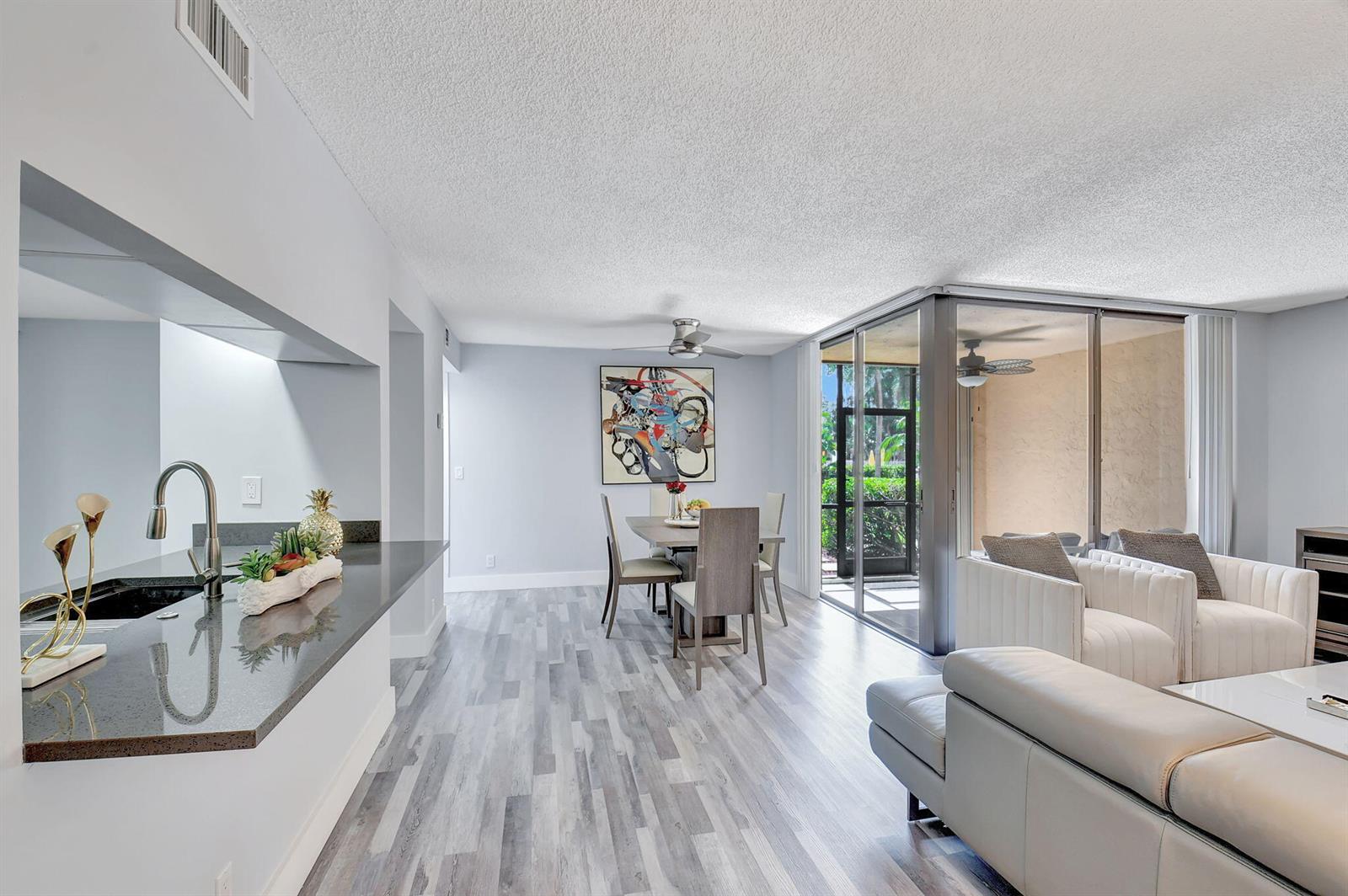 An open-concept living and dining area features gray wood-look flooring and a kitchen pass-through window — 2255 Lindell Boulevard # 4103, Delray Beach FL 33444, DELRAY BEACH, FL