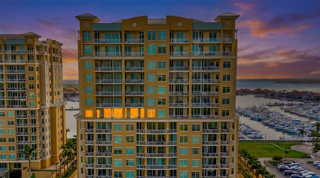 An exterior view of a tall, multi-story residential building overlooking a marina at sunset — 130 RIVIERA DUNES WAY UNIT 804, PALMETTO, FL