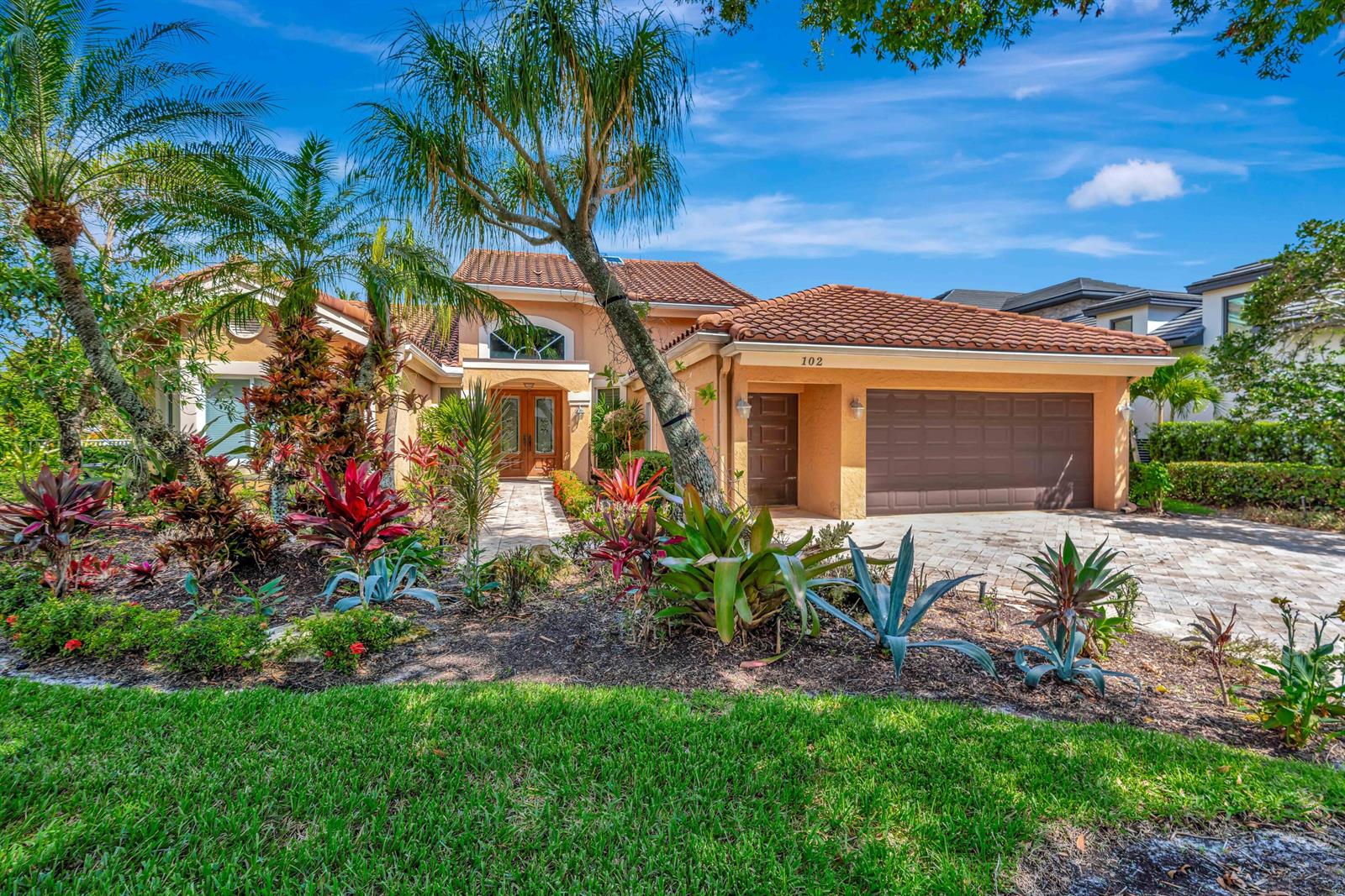 A single-story house with a tile roof, a two-car garage, and lush tropical landscaping — 102 Victory Drive, Jupiter FL 33477, JUPITER, FL