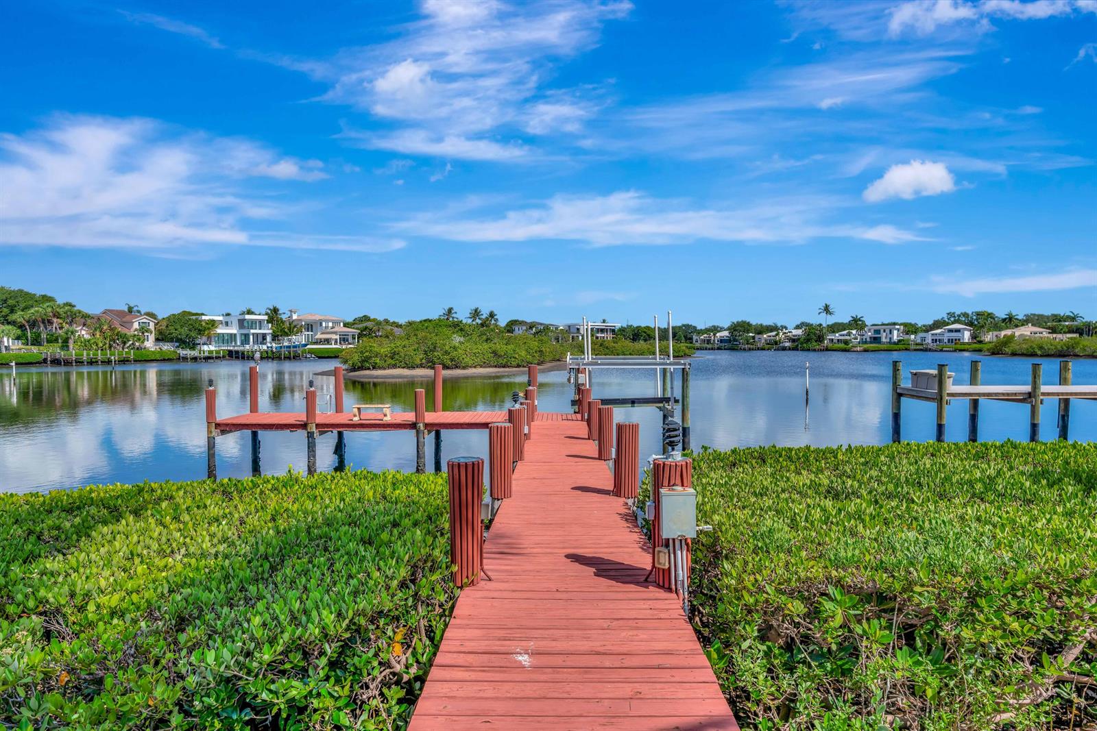 A wooden dock extends over a calm waterway surrounded by lush green mangroves and houses — 102 Victory Drive, Jupiter FL 33477, JUPITER, FL