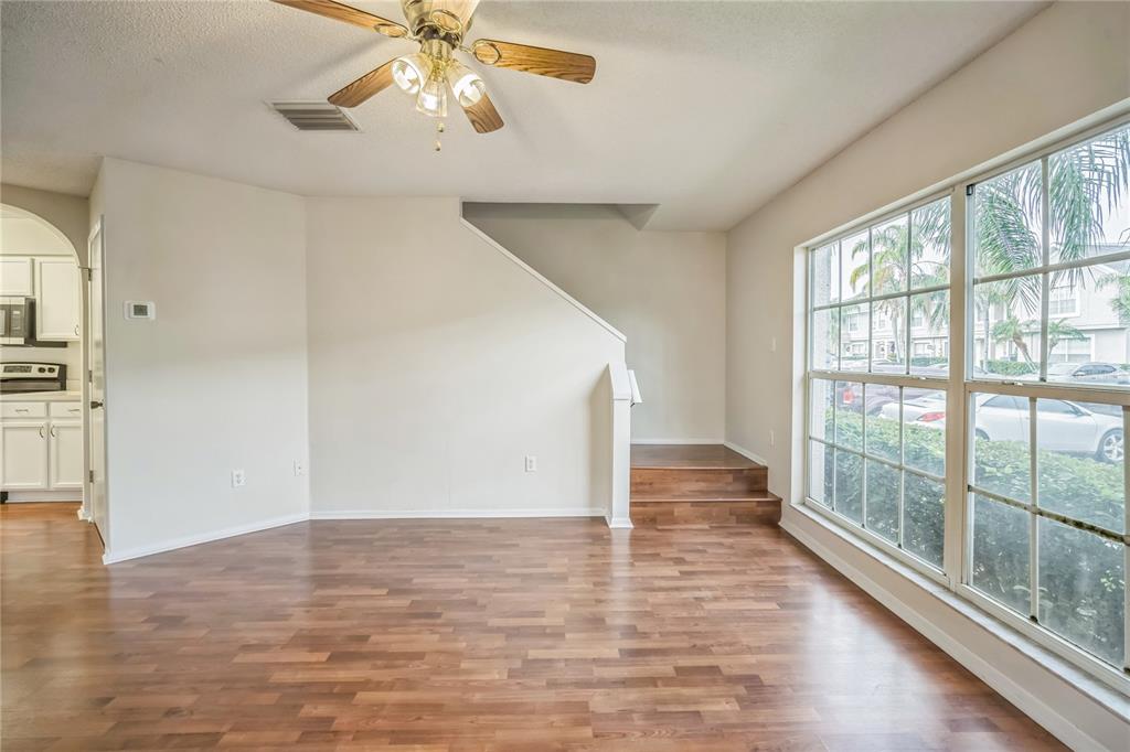 A living room with wood flooring, a ceiling fan, and stairs leading to an upper level — 523 KENSINGTON LAKE N, BRANDON, FL