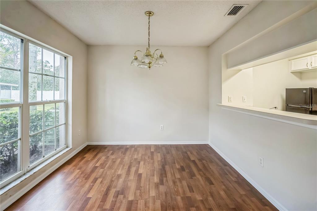 An empty dining room with wood-look flooring, a chandelier, and a pass-through to the kitchen — 523 KENSINGTON LAKE N, BRANDON, FL