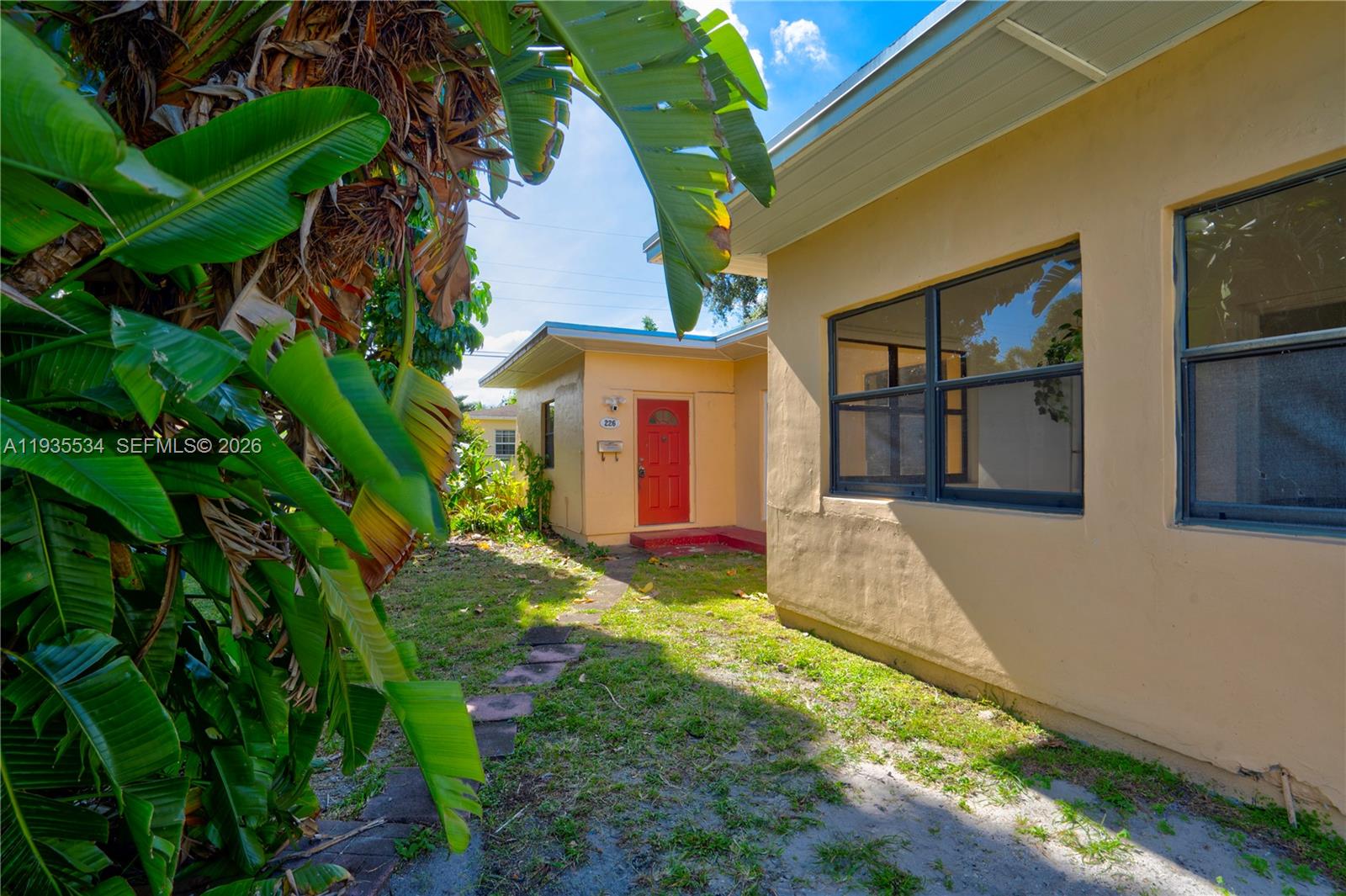 A tan exterior wall with a red door and a stone path in the yard — 234 NE 111th St # 1, Miami FL 33161, MIAMI, FL
