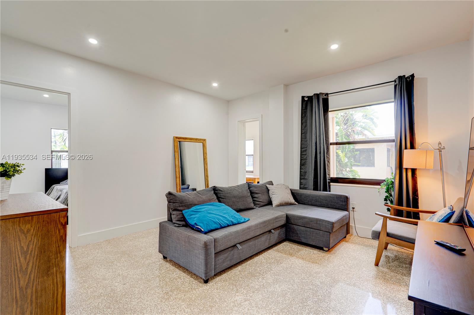 A living room features a gray sectional sofa, a floor mirror, and a window with curtains — 234 NE 111th St # 1, Miami FL 33161, MIAMI, FL