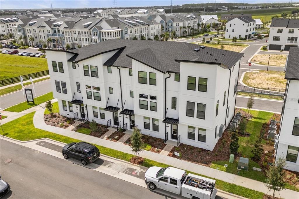 An aerial view of a modern white three-story townhouse with a black roof — 15489 HAMLIN PARK DRIVE, WINTER GARDEN, FL