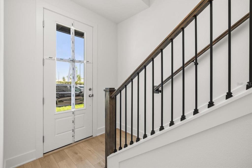An entryway features a white door, light wood flooring, and a staircase with black railings — 15489 HAMLIN PARK DRIVE, WINTER GARDEN, FL