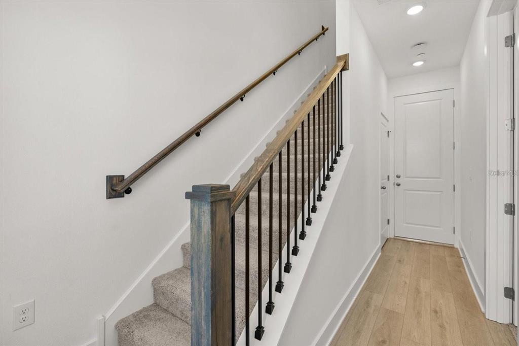 A carpeted staircase with a wooden handrail and black metal balusters leads to a hallway — 15489 HAMLIN PARK DRIVE, WINTER GARDEN, FL