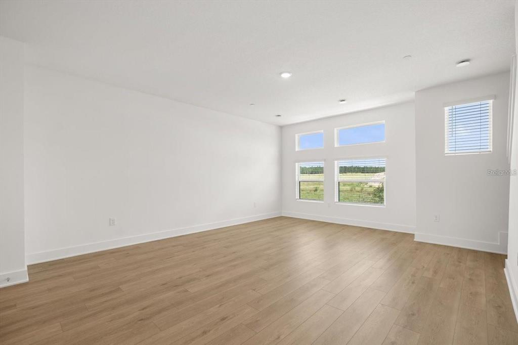 An empty room with white walls, light wood flooring, and several windows — 15489 HAMLIN PARK DRIVE, WINTER GARDEN, FL