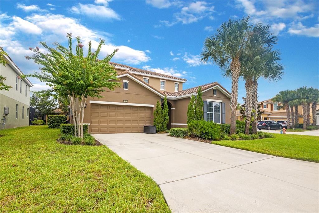 A two-story tan house with a two-car garage, palm trees, and a concrete driveway — 5207 WILDWOOD WAY, DAVENPORT, FL