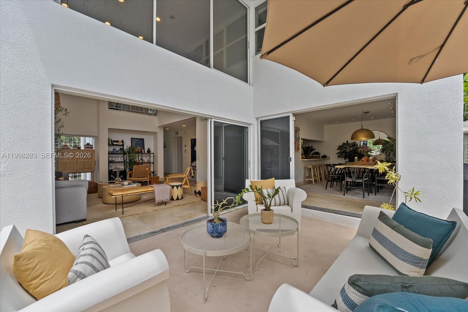A patio with white furniture and two round tables overlooks an open-concept living and dining area — 2721 SW 22nd Ave # A, Miami FL 33133, MIAMI, FL