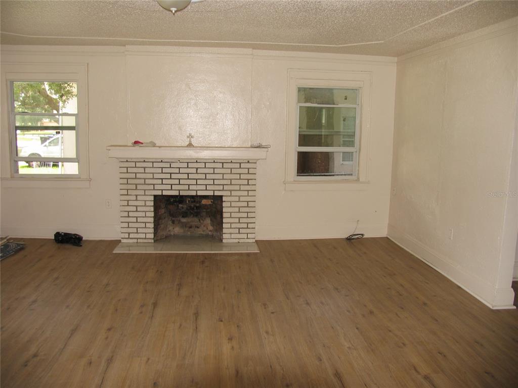 A living room features light wood-look flooring, a white brick fireplace, and two windows — 323 DOVER STREET, ORLANDO, FL
